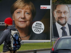 A man walks by election posters of German Chancellor Angela Merkel, left, and her challenger Martin Schulz from the Social Democrats in Frankfurt, Germany, Wednesday, Sept. 20, 2017. German elections will be held on upcoming Sunday. (AP Photo/Michael Probst)