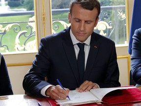 French President Emmanuel Macron signs documents in front of the media to promulgate a new labor bill in his office at the Elysee Palace in Paris, France, Friday, Sept. 22, 2017. Macron has signed Friday five decrees paving the way to the implementation of labor measures aimed at boosting growth, his first major reform since his election. (Philippe Wojazer/Pool Photo via AP)