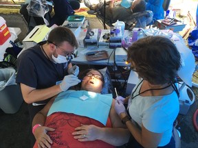 In this Friday, July 21, 2017 photo, dental student Carl Leiner, left, checks Lisa Kantsos teeth at the Remote Area Medical clinic in Wise, Va. Kantsos and hundreds of other uninsured patients came to the rural clinic for free dental and medical care. (AP Photo/Dylan Lovan)