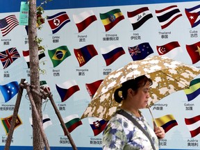 FILE - In this Sept. 4, 2017, file photo, a woman carries an umbrella past a board displaying countries' national flags in Beijing. A foreign business group appealed to China on Tuesday, Sept. 19, 2017, to move faster in carrying out promises to open its state-dominated economy and warned that inaction might fuel a backlash against free trade. Beijing faces mounting complaints from Washington and Europe about barriers in industries from finance to medical equipment while its own competitors have largely unfettered access to foreign markets. (AP Photo/Andy Wong, File)