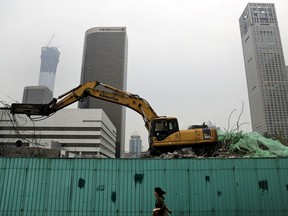 In this photo taken on Friday, Sept. 15, 2017, a woman walks by a machine demolish an old building at the Central Business District in Beijing. The Standard & Poor's rating agency cut China's credit rating on Thursday, Sept. 21, 2017 due to its rising debts, highlighting challenges faced by Communist leaders as they cope with slowing economic growth. (AP Photo/Andy Wong)