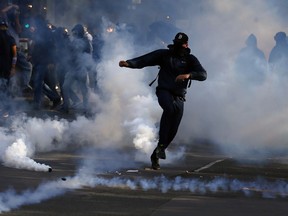 Masked protester runs in teargas during a protest march against President Emmanuel Macron's new pro-business labor policies in Paris, France, Thursday, Sept. 21, 2017. President Emmanuel Macron's presidency is facing its second big public test, as unions hold nationwide protests against changes to labor laws that they fear corrode hard-fought job security. (AP Photo/Francois Mori)