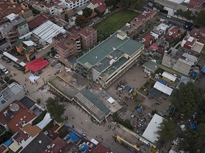 Volunteers and rescue workers search for one last person thought to be trapped inside the Enrique Rebsamen school, collapsed by a 7.1 earthquake in southern Mexico City, early evening Saturday, Sept. 23, 2017. As rescue operations stretched into day 5, residents throughout the capital have held out hope that dozens still missing might be found alive. There is a message written on top of the green surfaced building, that reads in Spanish "Silence, no helicopters." (AP Photo/Miguel Tovar)