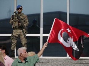 Under the watchful eye of a Turkish army soldier standing guard outside a court, protesters, one holding a Turkish flag with an image of Mustafa Kemal Ataturk, the founder of Modern Turkey, demonstrate against a trial of journalists and staff from the Cumhuriyet newspaper, accused of aiding terror organizations, in Silivri, Turkey, Monday, Sept. 11, 2017. The trial against journalists and staff from Cumhuriyet newspaper staunchly opposed to President Recep Tayyip Erdogan continues in Istanbul, a case that has added to concerns over rights and freedoms in Turkey. (AP Photo/Emrah Gurel)
