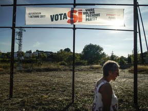 In this Wednesday, Oct. 4, 2017 photo, Guadalupe Espinosa passes by the only referendum sign in the city on the Catalan side at San Rafael del Rio, a small regional border-town some 207 kilometers (129 miles) south of Barcelona. Spain. The river that runs through San Rafael del Rio, a quiet rural town with a population of just over 500, provides a natural boundary between the Spanish regions of Catalonia and Valencia. Now residents are worried that the escalating conflict between Spanish and Catalan authorities will split the town in two. (AP Photo/Mstyslav Chernov)