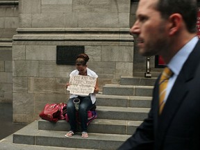 A business man walks by a homeless woman holding a card in New York City