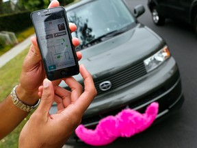 A driver for Lyft shows his phone with an incoming ride request in front of his car.