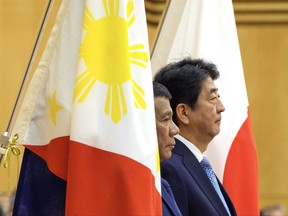 Philippine President Rodrigo Duterte, left, and Japanese Prime Minister Shinzo Abe stand between the countries' flags as they review a guard of honor at Abe's official residence in Tokyo Monday, Oct. 30, 2017. Duterte is on a two-day visit to Japan. (Nicolas Datiche/Pool Photo via AP)