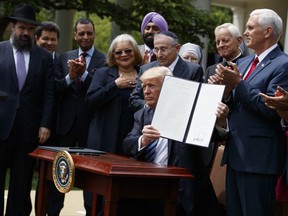 FILE - In this May 4, 2017 file photo, President Donald Trump holds up a signed executive order aimed at easing an IRS rule limiting political activity for churches in the Rose Garden of the White House in Washington.  In an order that undercuts federal protections for LGBT people, Attorney General Jeff Sessions issued a sweeping directive to agencies Friday to do as much as possible to accommodate those who claim their religious freedoms are being violated.  Trump announced plans for the directive last May in a Rose Garden ceremony where he was surrounded by religious leaders. Since then, religious conservatives have anxiously awaited the Justice Department guidance.  (AP Photo/Evan Vucci)