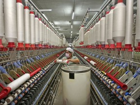 In this Oct. 20, 2017 photo, a worker prepares to load a cotton thread barrel into the machine at a textile factory in Huaibei in central China's Anhui province. Chinese manufacturing activity expanded in October at a slower pace than the previous month as output weakened on softer demand in the world's No. 2 economy, an official survey said Tuesday, Oct. 31. (Chinatopix via AP)