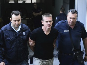 FILE - In this Wednesday, Oct. 4, 2017 file photo, police officers escort Alexander Vinnik, center, as they leave a courthouse at the northern Greek city of Thessaloniki. Russia has won the latest round in a judicial tug-of-war with the U.S. over who should try a Russian cybercrime suspect arrested during a holiday in Greece. (AP Photo/Giannis Papanikos, File)