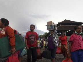 Villagers carry their belongings during an evacuation following the eruption of the Mount Agung, seen in the background, in Karangasem, Indonesia, Sunday, Nov. 26, 2017. The volcano on the Indonesian island of Bali has rumbled into life with a series of eruptions that temporarily disrupted some international flights to the popular tourist destination. (AP Photo/Firdia Lisnawati