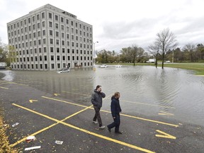 People walk past the flooded parking lot of the Pebb Building, located across from the Ottawa River, following a rain storm in Ottawa on Monday, Oct. 30, 2017. The National Research Council says Canada's homes and highways were built with assumptions about weather patterns that are no longer relevant thanks to climate change. THE CANADIAN PRESS/Justin Tang