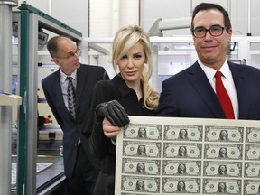 Treasury Secretary Steven Mnuchin, right, and his wife Louise Linton, hold up a sheet of new $1 bills, the first currency notes bearing his and U.S. Treasurer Jovita Carranza's signatures, Wednesday, Nov. 15, 2017, at the Bureau of Engraving and Printing (BEP) in Washington. The Mnuchin-Carranza notes, which are a new series of 2017, 50-subject $1 notes, will be sent to the Federal Reserve to issue into circulation. At left is BEP Director Leonard Olijar. (AP Photo/Jacquelyn Martin)