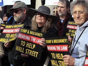 Guy Brandenburg, from left, and Barbara Heil, hold banners with other protesters during a rally outside the Consumer Financial Protection Bureau headquarters in Washington, Tuesday, Nov. 28, 2017. The group were protesting President Donald Trump's appointment of Mick Mulvaney as Consumer Financial Protection Bureau's acting director. (AP Photo/Manuel Balce Ceneta)