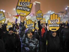 People hold signs that read "All for Justice" during a protest outside the government headquarters in Bucharest, Romania, Sunday, Nov. 26, 2017. Thousands of Romanians have gathered in Bucharest and other cities to protest against government plans to introduce legislation they say will weaken efforts to root out corruption. (AP Photo/Vadim Ghirda)