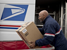 A letter carrier lifts an Amazon.com Inc. package from a bin while preparing a vehicle for deliveries at the United States Postal Service in Washington, D.C.