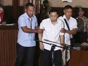 Former speaker of Indonesia's parliament Setya Novanto, center, walks as he is escorted by investigators during his trial in Jakarta, Indonesia, Wednesday, Dec. 13, 2017.  The top Indonesian politician accused of involvement in one of the country's biggest corruption scandals told a court on the first day of his trial he's suffering a stomach complaint, forcing a postponement while his medical condition is checked.
