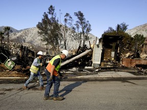 Workers from the Los Angeles Dept. of Water and Power walk past a home destroyed by wildfire along Via San Anselmo in the Sylmar area of Los Angeles Wednesday, Dec. 6, 2017.