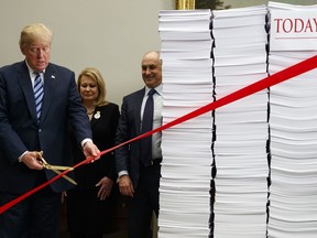 President Donald Trump cuts a ribbon during an event on federal regulations in the Roosevelt Room of the White House, Thursday, Dec. 14, 2017, in Washington. "Let's cut the red tape, let's set free our dreams," Trump said as he symbolically cut a ribbon on stacks of paper representing the size of the regulatory code.