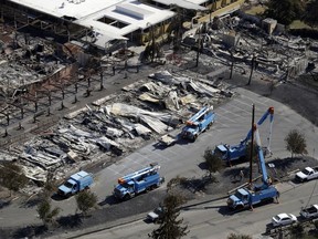 File - In this Oct. 14, 2017 file photo, Pacific Gas & Electric crews work on restoring power lines in a fire ravaged neighborhood in an aerial view in the aftermath of a wildfire in Santa Rosa, Calif. California utility regulators are considering tougher safety rules for power lines, phone lines and utility poles in parts of the state that are prone to fires. The rules being taken up Thursday, Dec. 14, 2017, would require tree branches to be kept farther away from power lines and newly installed lines to be spaced farther apart.