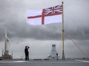 In this photo taken on Dec. 7, 2017, a naval officer looks up at the White ensign flag flying at the stern of the navy's new flag ship the aircraft carrier "HMS Queen Elizabeth" which was commissioned into the Royal navy, in Portsmouth. The British navy's newest and most expensive aircraft carrier needs repairs after a faulty shaft seal was identified during sea trials, it was reported on Tuesday, Dec. 19, 2017.
