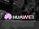 People walk past an illuminated logo for Huawei in Beijing. 
