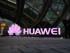 People walk past an illuminated logo for Huawei in Beijing.