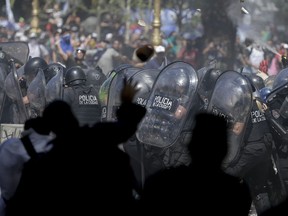 Police take cover from stones thrown by demonstrators during a general strike and protest against a pension reform measure in Buenos Aires, Argentina, Monday, Dec. 18, 2017. Union leaders complain the legislation, which already passed in the Senate, would cut pension and retirement payments as well as aid for some of poor families.