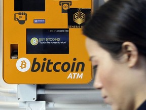 FILE - In this Dec. 21, 2017 file photo, a woman walks past the Bitcoin ATM in Hong Kong. The growth of bitcoin is fueling speculation about the environmental impact of the energy needed to power the cryptocurrency, stemming from the process of "mining," which is central to its existence.