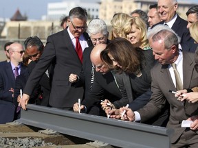 FILE - In this Jan. 6, 2015, file photo, Gov. Jerry Brown, center, and his wife, Anne Gust Brown, fourth from right, sign a portion of a rail at the California High-Speed Rail Authority groundbreaking event as Gina McCarthy, administrator of the U.S. Environmental Protection Agency, standing next to Brown at left, watches in Fresno, Calif. A bipartisan team of lawmakers are seeking a formal audit of California's high-speed rail project following a nearly $3 billion jump in costs. Democratic Sen. Jim Beall and Republican Assemblyman Jim Patterson will make their pitch for the audit Tuesday, Jan. 30, 2018, to a joint committee that will choose whether to authorize it.