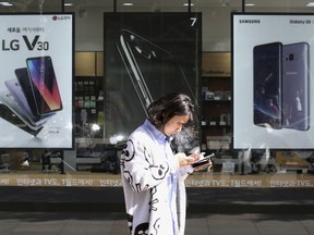 FILE - In this Tuesday, Oct. 17, 2017 file photo, a woman walks by posters adverting smartphones at a mobile phone shop in Seoul, South Korea. Researchers have completed the first survey of valuable materials they say are waiting to be mined from Europe's vast landfills and scrapyards. A group of 17 organizations on Wednesday, Jan. 17, 2018 launched an online database for 'urban mining' detailing precious raw materials slumbering in discarded batteries, electronics and cars across the continent. Smartphones have concentrations of gold that are more than 25 times as high as the richest underground ores and are far easier to extract.