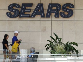FILE - In this Aug. 31, 2017, file photo, shoppers walk by the sign at a Sears store in Pittsburgh. Sears is raising $100 million in new financing, will seek twice that from other sources, and will attempt $200 million in additional cost cuts in 2018, unrelated to store closings.