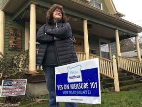 In this Friday, Jan. 19, 2018, photo, Kelly Burke poses for a photo outside her home next to a sign supporting Oregon's Measure 101 in Portland, Ore. Burke has volunteered for phone banks to garner support for the measure that goes before Oregon voters on Tuesday, Jan. 23.