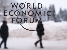 Two persons walk behind the logo of the World Economic Forum at the meeting's conference center in Davos, Switzerland, Sunday, Jan. 21, 2018. One question looms as President Donald Trump packs his bags and heads for the mountains of Switzerland later this week: How will the diet Coke-loving nationalist fit in with the champagne-swilling globalists he'll encounter at the World Economic Forum in Davos?