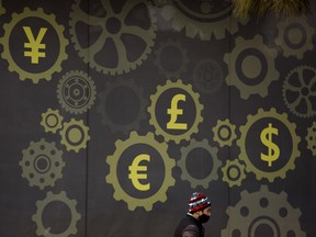 FILE - In this Jan. 18, 2018, file photo, a deliveryman wearing a face mask walks past a display showing symbols for world currencies on the exterior of a bank in Beijing. Chinese authorities are struggling to quell protests following the collapse of an investment scheme police say took as much as $4.7 billion from millions of depositors.