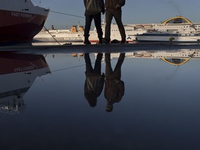Pedestrians are reflected in water in front of docked ferries at the port of Piraeus near Athens during a 24-hour strike, Friday, Jan. 12, 2018. Greek transport workers, doctors in public hospitals and seamen are in a 24-hour strike against Greece's government new batch of creditor-demanded reforms.