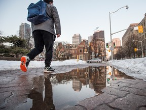 A man walks past a condo tower under construction reflected in water in Toronto.