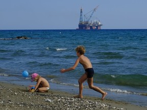 In this photo taken on Sunday, Oct. 15, 2017 children play on a beach with a drilling platform seen in the background, on the outskirts of Larnaca port, in the eastern Mediterranean island of Cyprus. Turkish warships on maneuvers in the Mediterranean Sea have blocked a rig belonging to the Italian energy firm ENI from reaching an area off Cyprus to start searching for gas, officials said Saturday, Feb. 10, 2018. Cyprus' Foreign Minister Ioannis Kasoulides told state broadcaster RIK that the rig has halted its journey heading south of Cyprus and was waiting for directions from ENI. He says Cypriot authorities are in contact with the company and the Italian government.