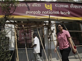 FILE- In this Monday, Feb. 19, 2018 file photo, people walk past a Punjab National Bank branch after it was sealed by the Central Bureau of Investigation in Mumbai, India. India's federal investigating agency says it has arrested six people in an alleged $1.8 billion bank fraud case. Abhished Dayal, a Central Bureau of Investigation spokesman, said Tuesday that five bank workers and an employee of billionaire jeweler and suspect Nirav Modi were arrested for allegedly conspiring to cheat the Punjab National Bank over the past six years.