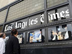 FILE - In this May 16, 2016, file photo, pedestrians look at news photos posted outside the Los Angeles Times building in downtown Los Angeles. The Los Angeles Times is reporting its parent company is in talks to be sold to local billionaire physician Patrick Soon-Shiong. The Washington Post first reported Tuesday, Feb. 6, 2018 that the sale was being negotiated by Tronc Inc., formerly Tribune Publishing. The Times then reported that the price was $500 million and would include the San Diego Union-Tribune. Chicago-based Tronc owns 10 U.S. newspapers.