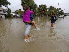 FILE - In this June 21, 2017 file photo, Don Noel carries his daughter Alexis, 8, with his wife Lauren, right as they walk through a flooded roadway to check on their boat in the West End section of New Orleans. The city of New Orleans is perhaps one of the best examples of what President Donald Trump calls the country's "crumbling infrastructure." But city officials have raised doubts about whether the president's bold plan will help. New Orleans needs more than $11 billion to update key parts of its infrastructure, and currently has only about $2 billion in hand.