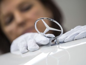 FILE - In this Jan. 24, 2018 file photo a woman fixes a Daimler Logo on a car at the Daimler AG company in Sindelfingen, Germany. Daimler AG says Thursday, Thursday, Feb. 1, 2018 its net profit rose 24 percent to a record 10.9 billion euros ($13.5 billion) last year, helped by strong sales of its Mercedes-Benz SUVs and new E-Class luxury sedan.