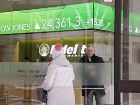 FILE- In this Feb. 6, 2018, file photo, a woman walks through the front doors at the Fidelity Investments office on Congress Street as the ticker displays stock market numbers in Boston. At Fidelity's retail brokerage customers continued to put in more buy orders than sells after the S&P 500 began falling from its peak set on Jan. 26, 2018. "Millennials and Gen Xers are definitely taking advantage of these prices and taking advantage of the sell-off," said Scott Ignall, senior vice president and head of online brokerage technology at Fidelity.