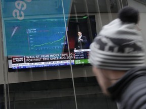 A pedestrian glances at a TV displaying financial news in Times Square, New York, Tuesday, Feb. 6, 2018. After big swings higher and lower, U.S. stocks are up slightly in afternoon trading Tuesday as investors look for calm after a global sell-off. The swings came one day after the steepest drop in 6 ½ years.