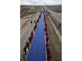 FILE - In this Saturday, March 10, 2018 file photo, Aymaras stand alongside a portion of a giant Bolivian Naval flag on the highway between Oruro and La Paz Bolivia. A narrow strip of blue stretched for more than 150 miles (nearly 200 kilometers) across the nation as part of a demonstration of the country's demand for an outlet to the sea. Land-locked Bolivia is calling on the International Court of Justice to order Chile to enter negotiations over granting Bolivia access to the Pacific Ocean.