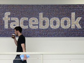 FILE - In this March 15, 2013, file photo, a Facebook employee walks past a sign at Facebook headquarters in Menlo Park, Calif. The San Jose Mercury News reports Saturday, March 17, 2018 that building permits compiled by Buildzoom show Facebook plans to erect the 465,000 square-foot (43,200 square-meter) building at its campus in Menlo Park, Calif.