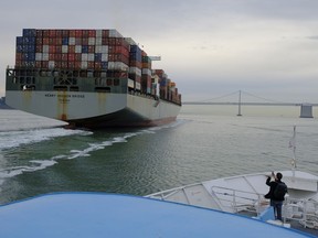 FILE- In this March 7, 2018, file photo, a man standing on the bow of a Golden Gate Ferry takes a picture of a container ship as it heads toward the San Francisco-Oakland Bay Bridge in San Francisco. On Wednesday, March 28, the Commerce Department issues its final estimate of how the U.S. economy performed in the October-December quarter.