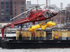 A helicopter is hoisted by crane from the East River onto a barge, Monday, March 12, 2018, in New York. The pilot was able to escape the Sunday night crash after the aircraft flipped upside down in the water killing several passengers, officials said.