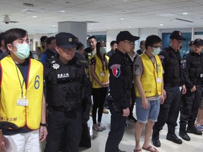 In this March 29, 2017, photo provided by Taiwan Criminal Investigation Bureau, Taiwan CIB SWAT team members stand with 18 suspects arrested upon arrival at Taoyuan International Airport in Taoyuan, Taiwan, when they were deported from Indonesia over telecom fraud. A joint effort by Taiwanese and Indonesian police resulted in the arrest of the 18 Taiwan nationals who were involving in cybercrime in Jakarta, Indonesia. Gangs operating from bases as far flung as Cambodia and Kenya, taking advantage of closer global connections and falling technology costs, are a growing source of tension between Beijing and the self-ruled island of Taiwan. (Taiwan Criminal Investigation Bureau via AP)